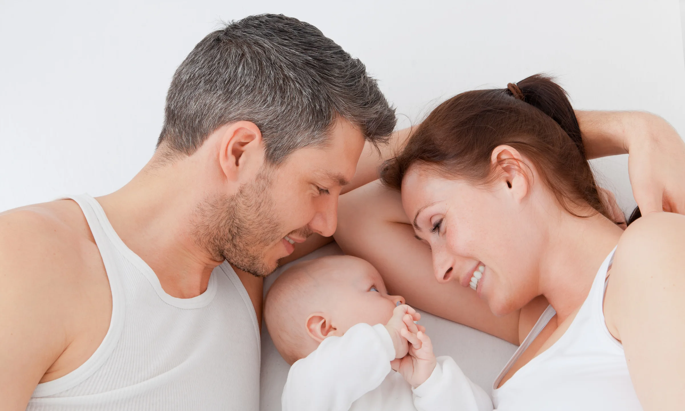 Eine Szene von drei Personen, die sich liebevoll anblicken: ein Mann, eine Frau, ein Baby. Paare oder Frauen: Die Praxis am Kudamm begleitet auf dem Weg zum Wunschkind.
