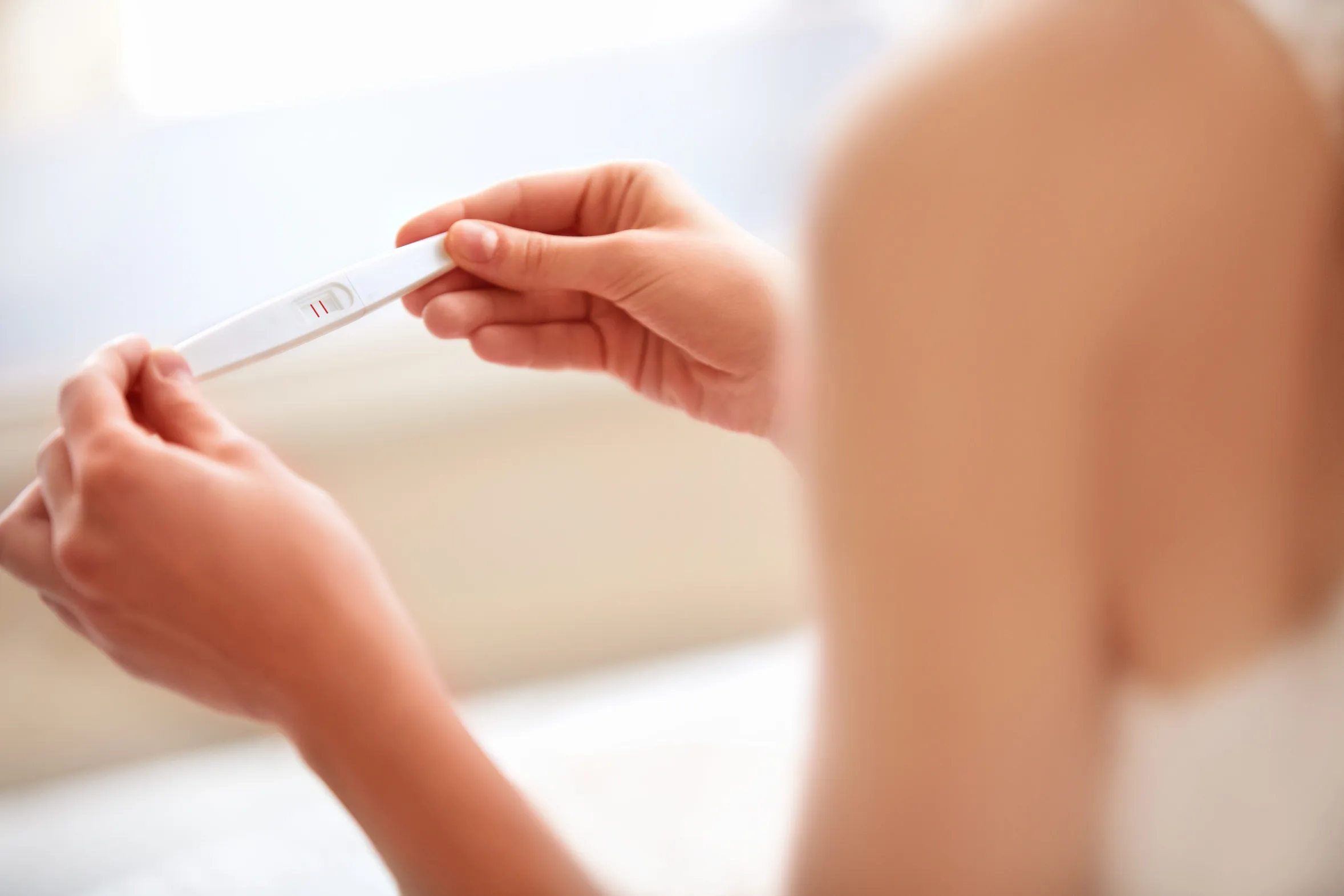 A woman holds a rapid pregnancy urine test with both hands, showing two continuous lines.