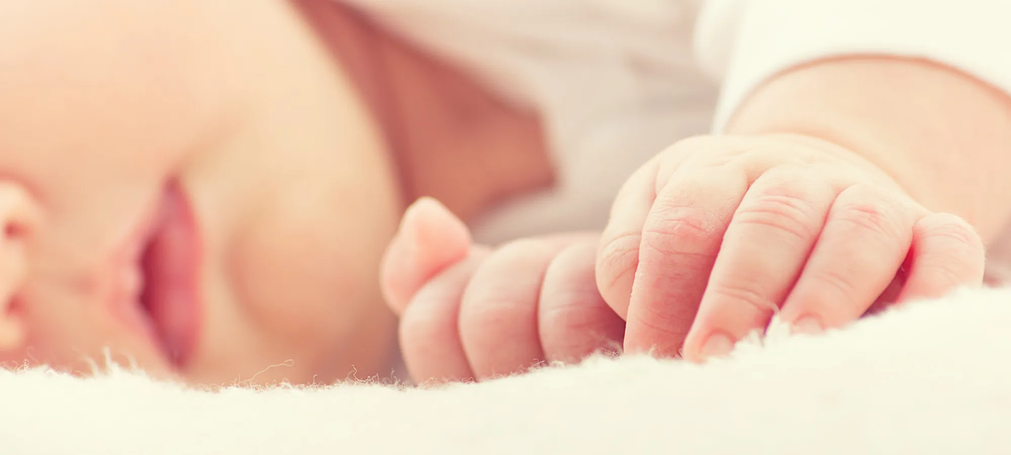 Ein schlafendes Baby liegt auf der Seite. Es trägt einen hellen Body und liegt auf einer flauschigen Unterlage.