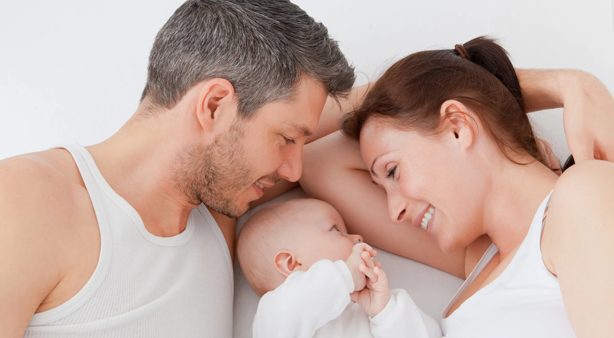 Ein Mann und eine Frau liegen sich gegenüber, in der Mitte ein Baby, das sein Gesicht der Frau zuwendet.