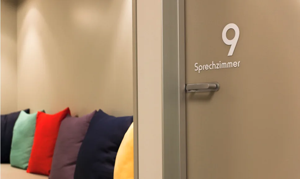 Sitzecke neben einer Tür, die mit "Sprechzimmer" und der Nummer "9" beschriftet ist.